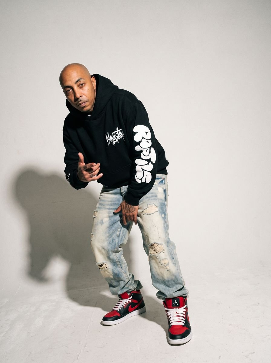 Man posing mid-step in a black hoodie, bleached denim and high-top sneakers